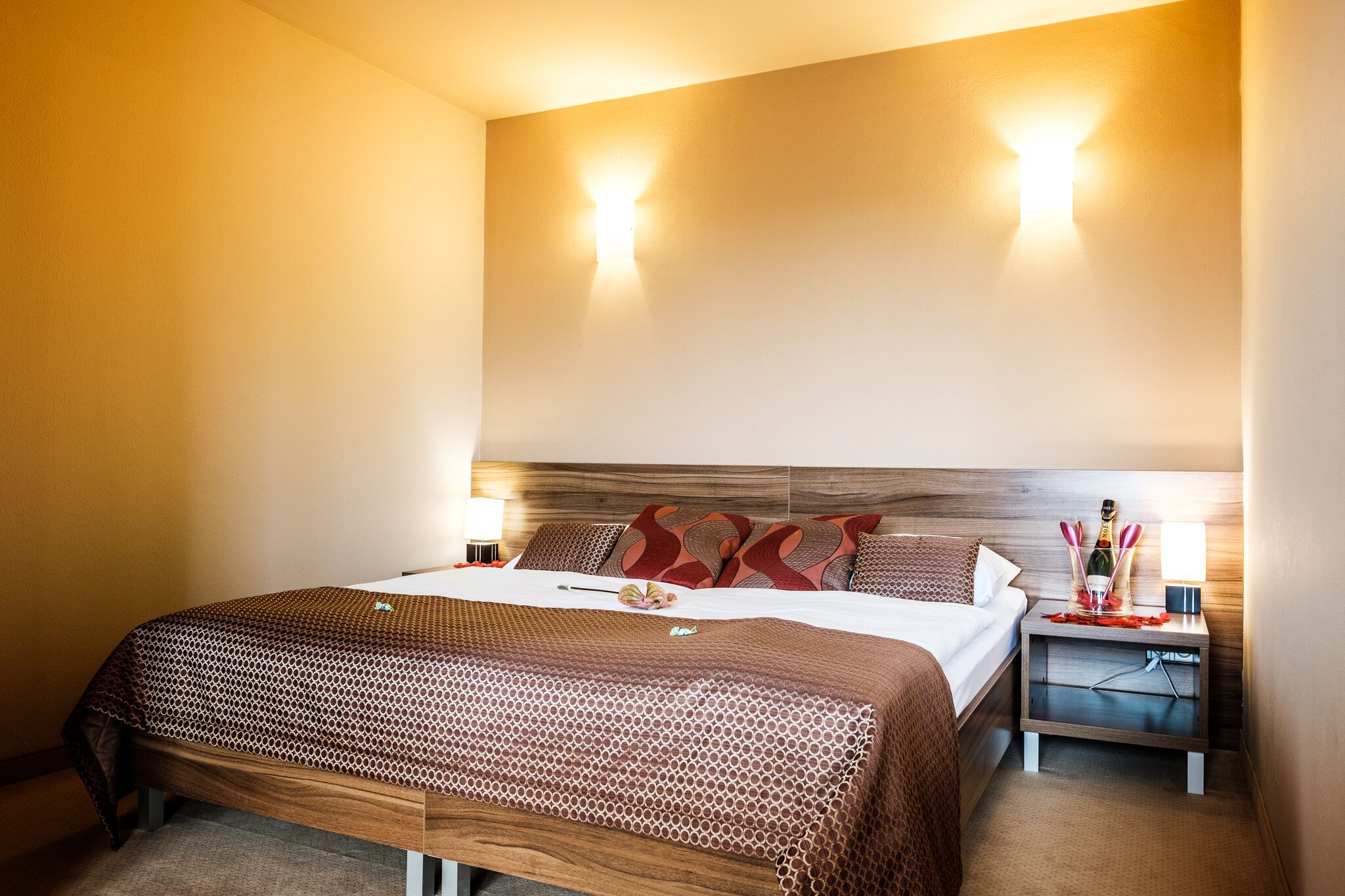 A hotel room with a large bed, two bedside tables with lamps, and a headboard with built-in lighting.