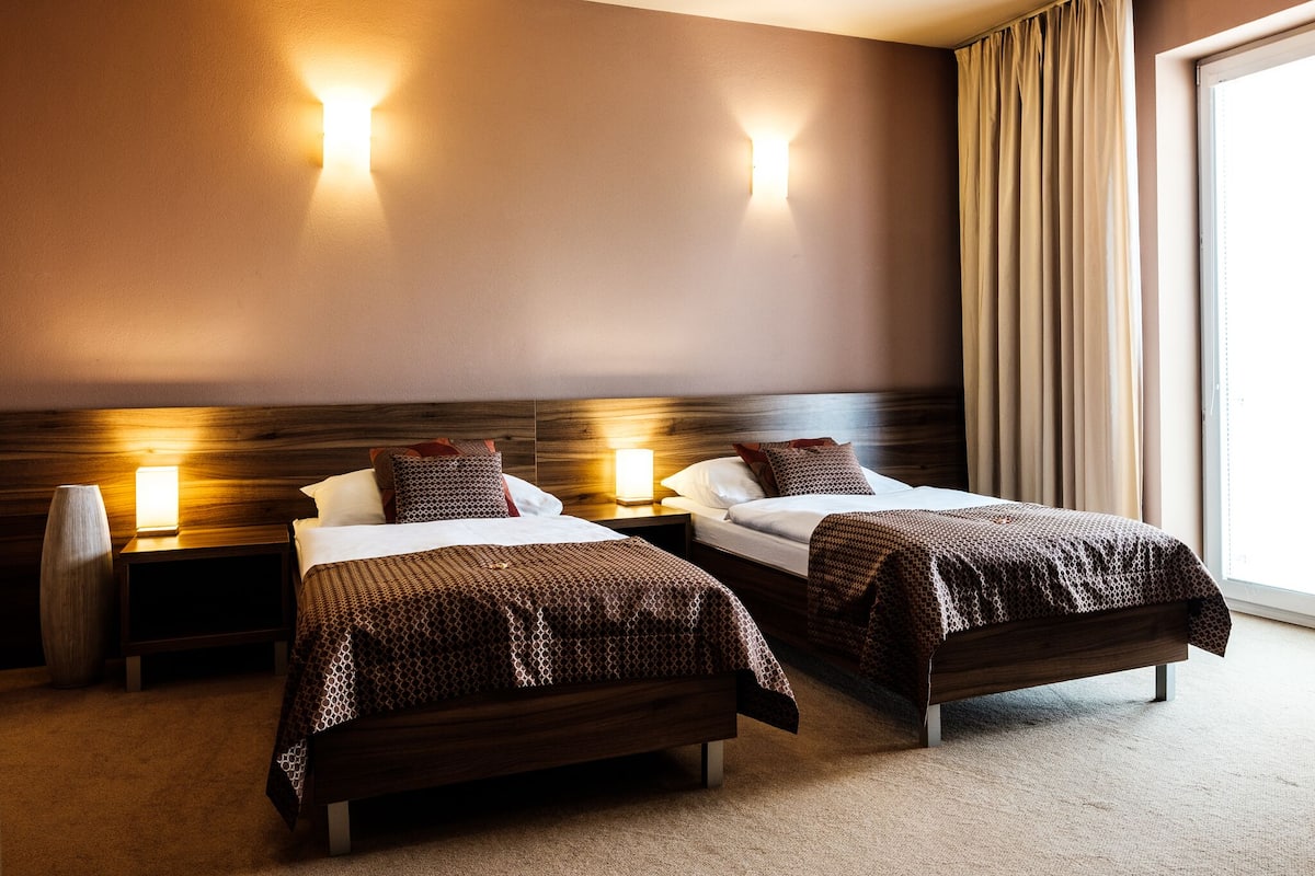 A hotel room with two beds, nightstands, and wall-mounted lights.