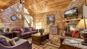 Un acogedor interior de cabaña de madera con una escalera, sofás de cuero, una mesa de centro y una chimenea.