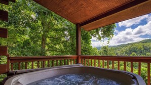 Un jacuzzi con terraza de madera y una vista panorámica de un área boscosa.