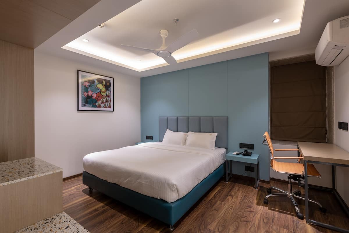 A modern hotel room with a bed, desk, chair, and ceiling fan.