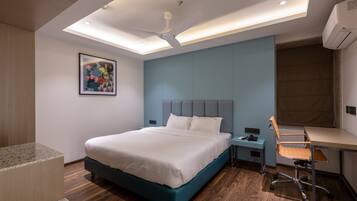 A modern hotel room with a bed, desk, chair, and ceiling fan.