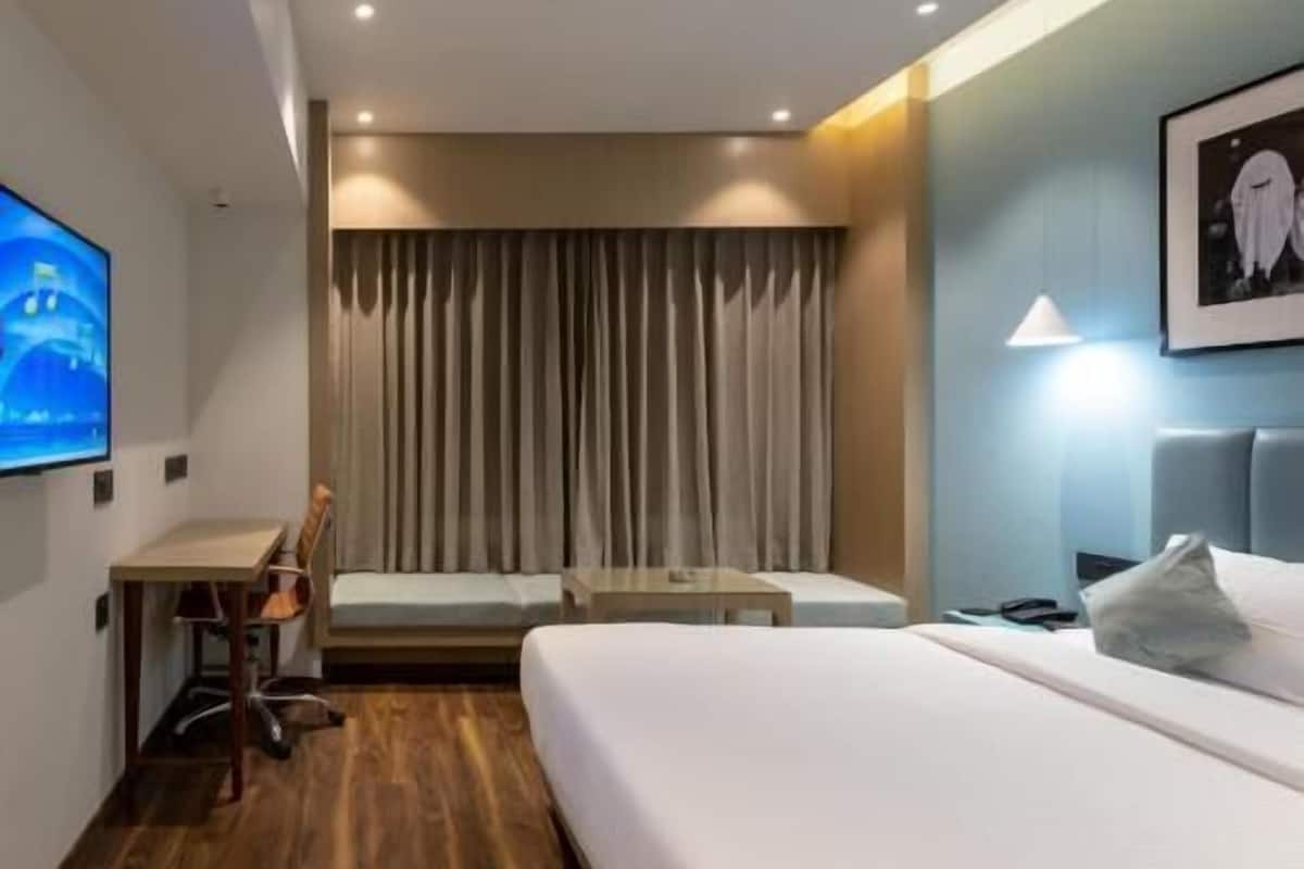 A hotel room with a bed, a desk, a chair, a television, and a curtain.