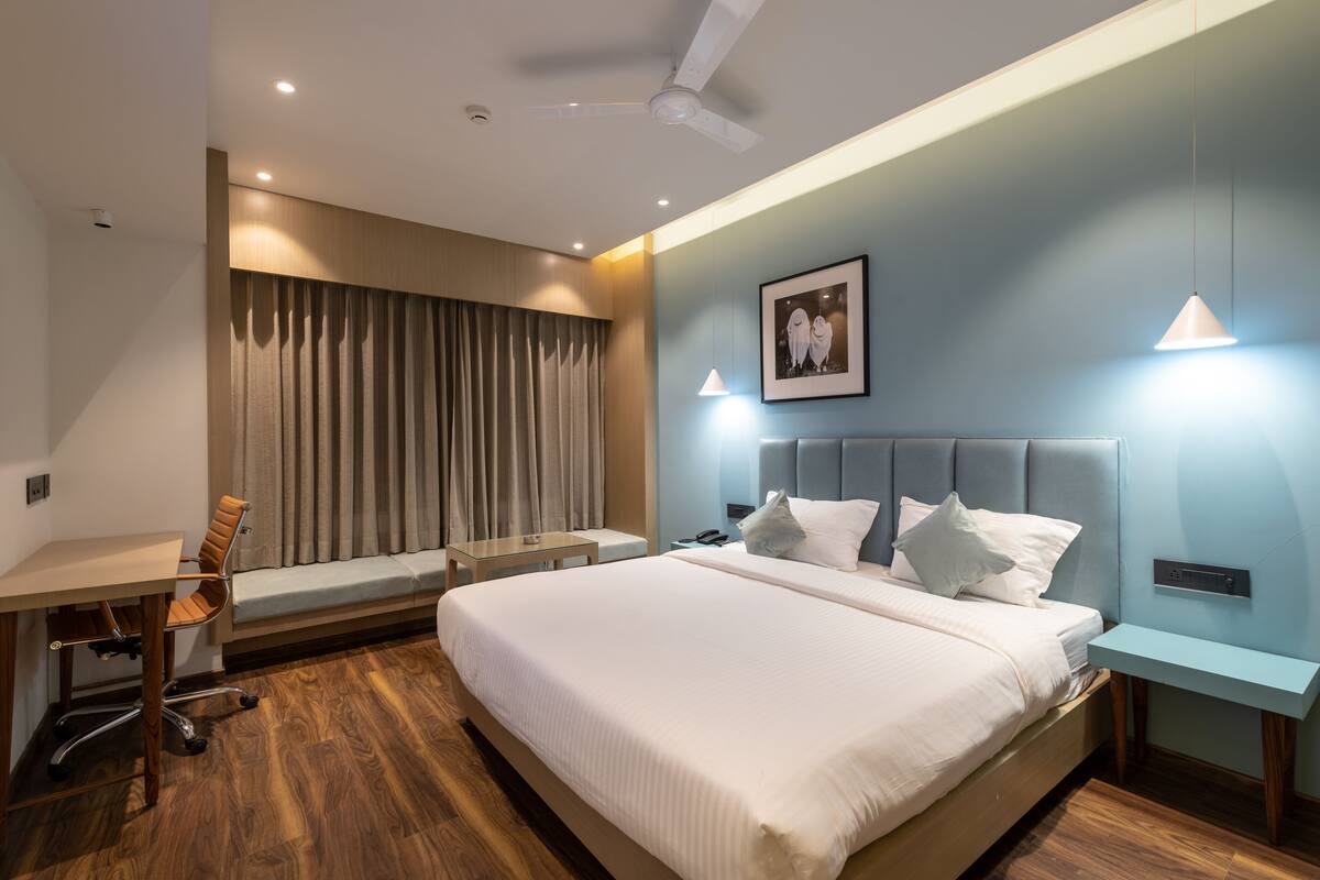A modern hotel room with a large bed, a desk, a chair, a sofa, and a ceiling fan.
