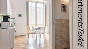 Een moderne keuken met witte apparaten, een eethoek met een tafel en stoelen, en een uitzicht op een stadsbeeld door grote ramen.