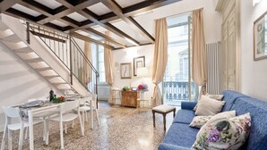 Un vaste espace de vie comprenant un escalier, une table à manger pour quatre personnes, un canapé bleu et une vue sur le balcon extérieur.