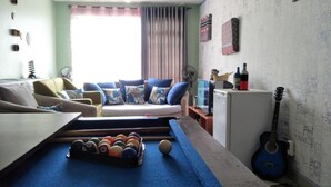 A living room with a pool table, a sofa, a small refrigerator, and a guitar. - Cozy Room JKIA (Mlolongo)