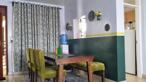 A dining area with a wooden table and two green chairs, a water dispenser, and decorative plates on the wall. - Cozy Room JKIA (Mlolongo)