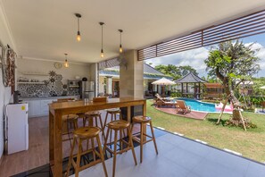 A modern kitchen with a bar area, a pool, and a view of the surrounding landscape. - Ayuna Suites Canggu By Zuzu (Tibubeneng)
