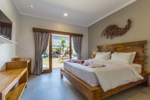 A modern bedroom with a wooden bed, a wooden desk, and a view of an outdoor area with a pool and chairs. - Ayuna Suites Canggu By Zuzu (Tibubeneng)