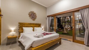 A modern bedroom with a wooden bed, a nightstand, and a view of a garden through a glass door. - Ayuna Suites Canggu By Zuzu (Tibubeneng)