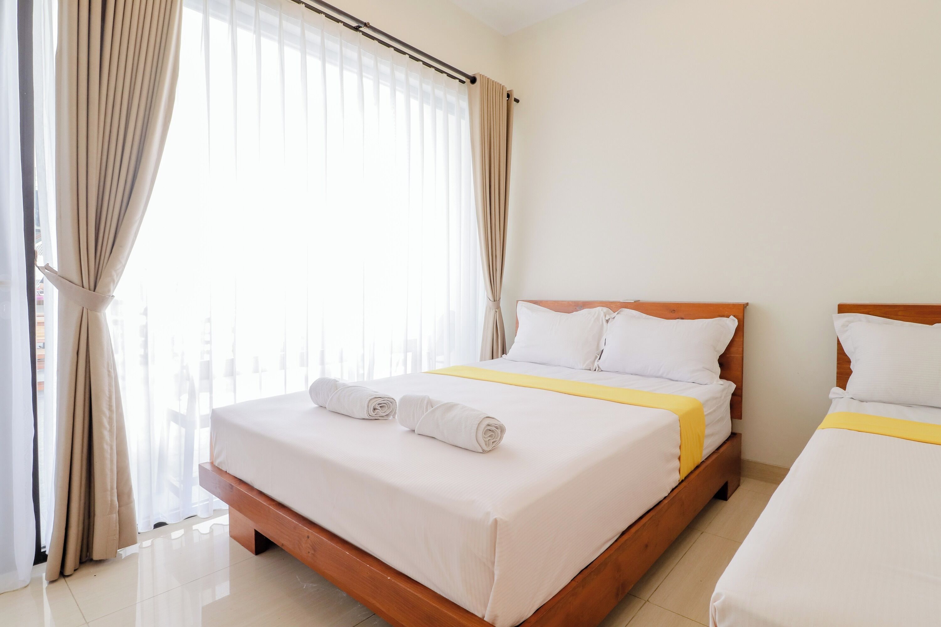 A hotel room with two beds, a wooden headboard, white linens, and a yellow bedspread.