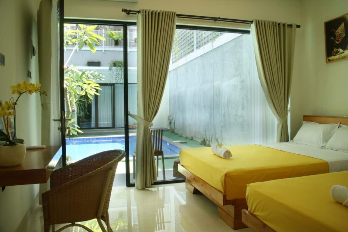 A hotel room with two beds, a small table, a chair, and a view of a swimming pool.