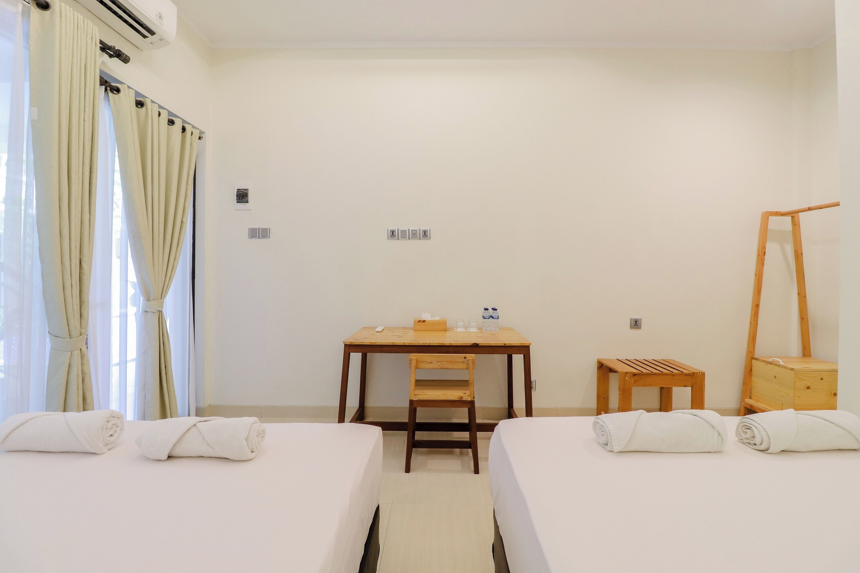 Habitación de hotel con dos camas, un escritorio, una silla, un taburete de madera y un armario de madera.
