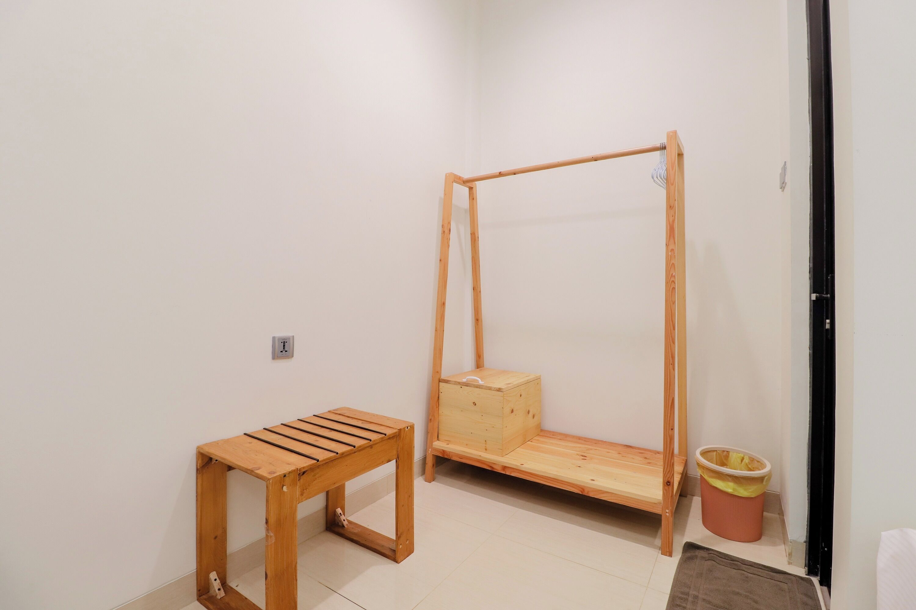 A room with a wooden bed frame, a small wooden table, and a trash bin.
