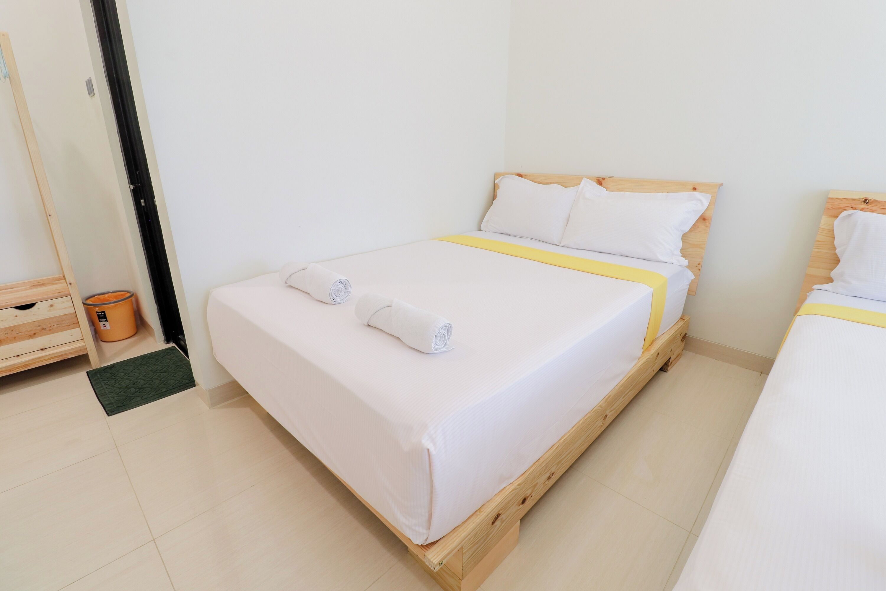 A single bed with a wooden frame, white bedding, and a yellow accent.