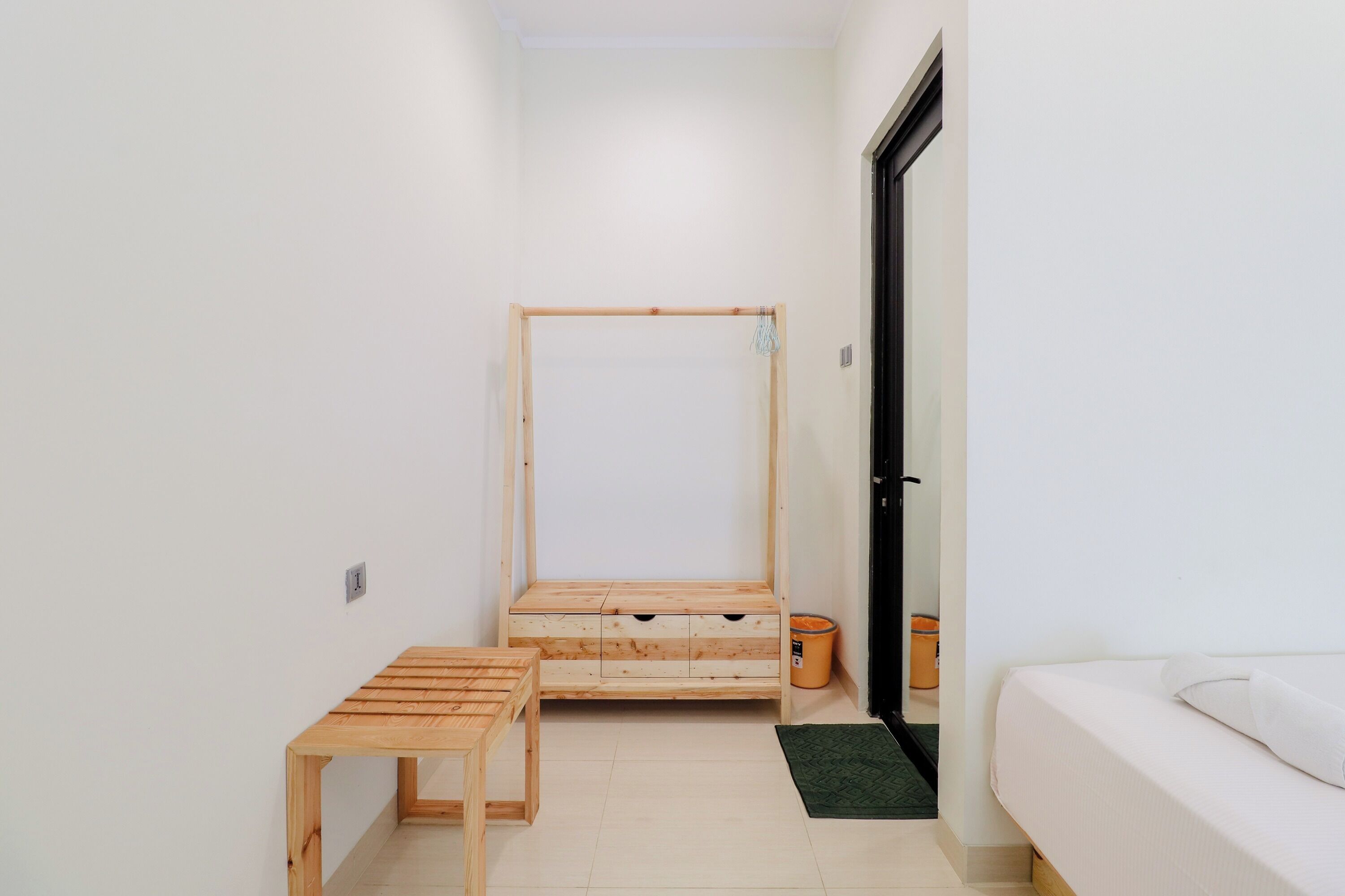 Una habitación pequeña y limpia con una cama de madera, una mesita y un banco de madera.