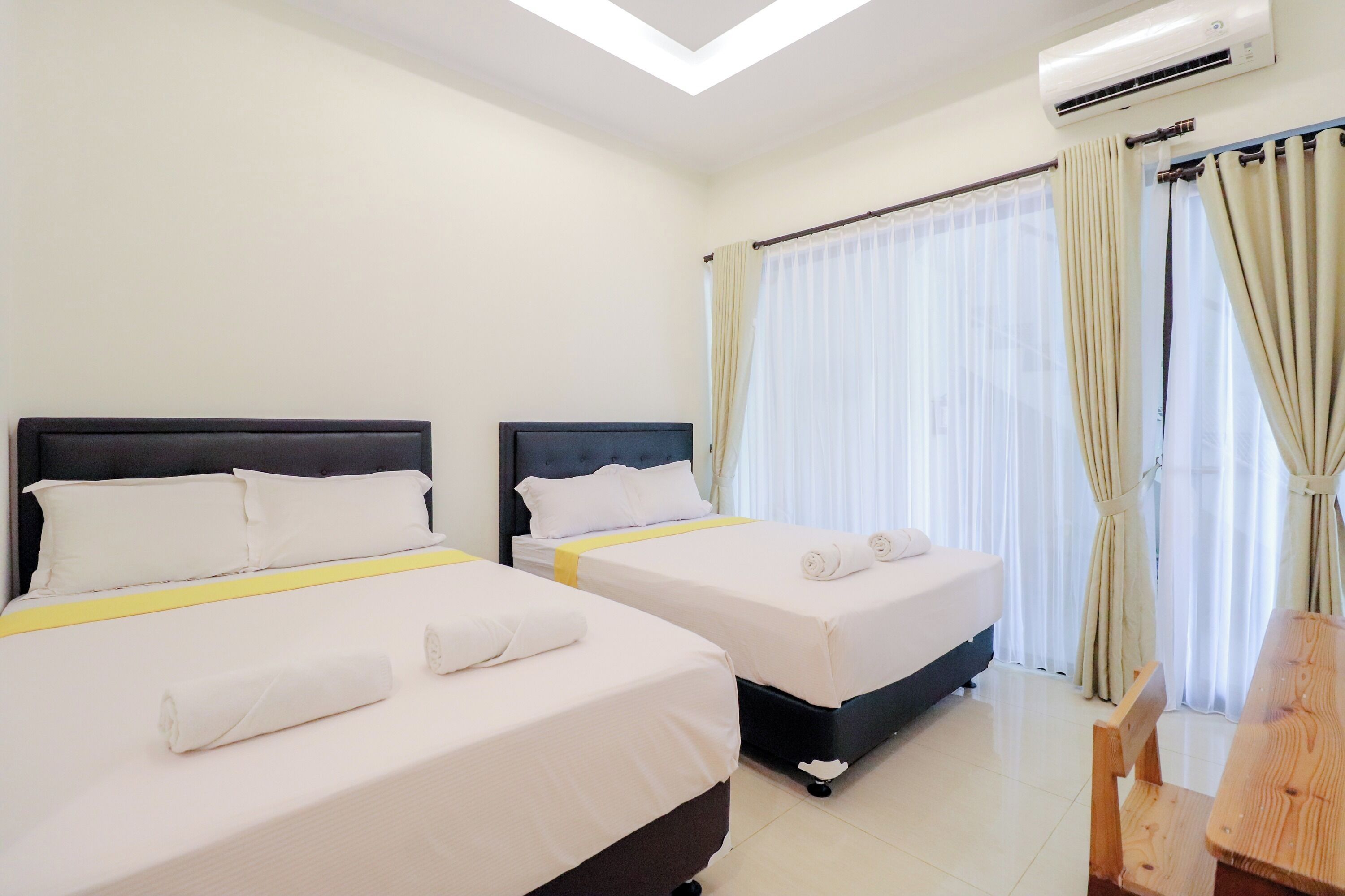A hotel room with two beds, a wooden chair, and a window with curtains.