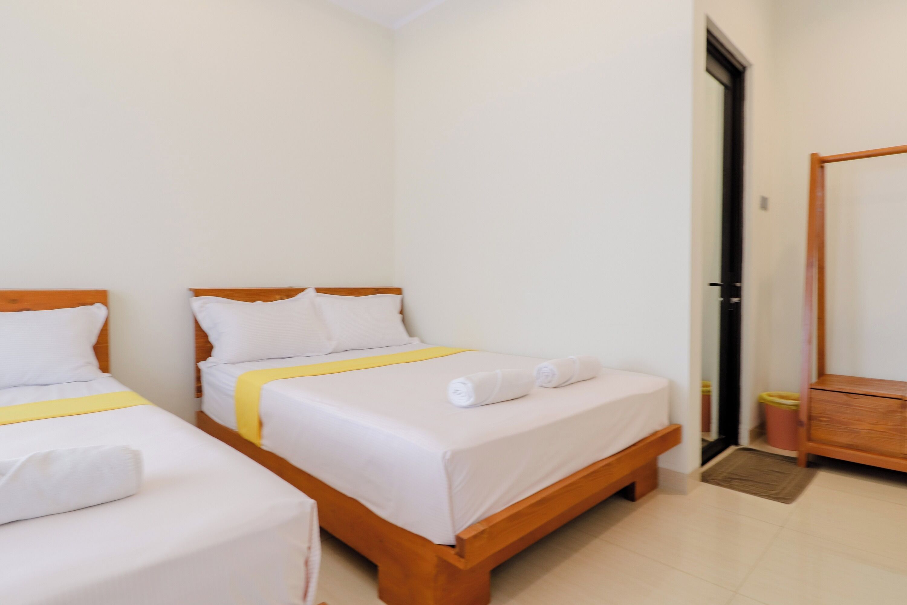 A hotel room with two single beds, a wooden wardrobe, and a door leading to another room.