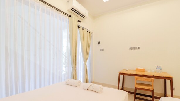 A hotel room with a bed, a desk, and a chair. There is an air conditioning unit above the bed. - Roemah Kenari (Yogyakarta)