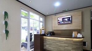 A reception area with a wooden reception desk, a television mounted on the wall, and a large window providing natural light. - I Residence Bandung (Bandung)