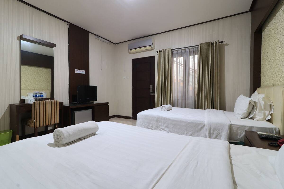 A hotel room with two beds, a desk with a TV, a mirror, and an air conditioning unit.