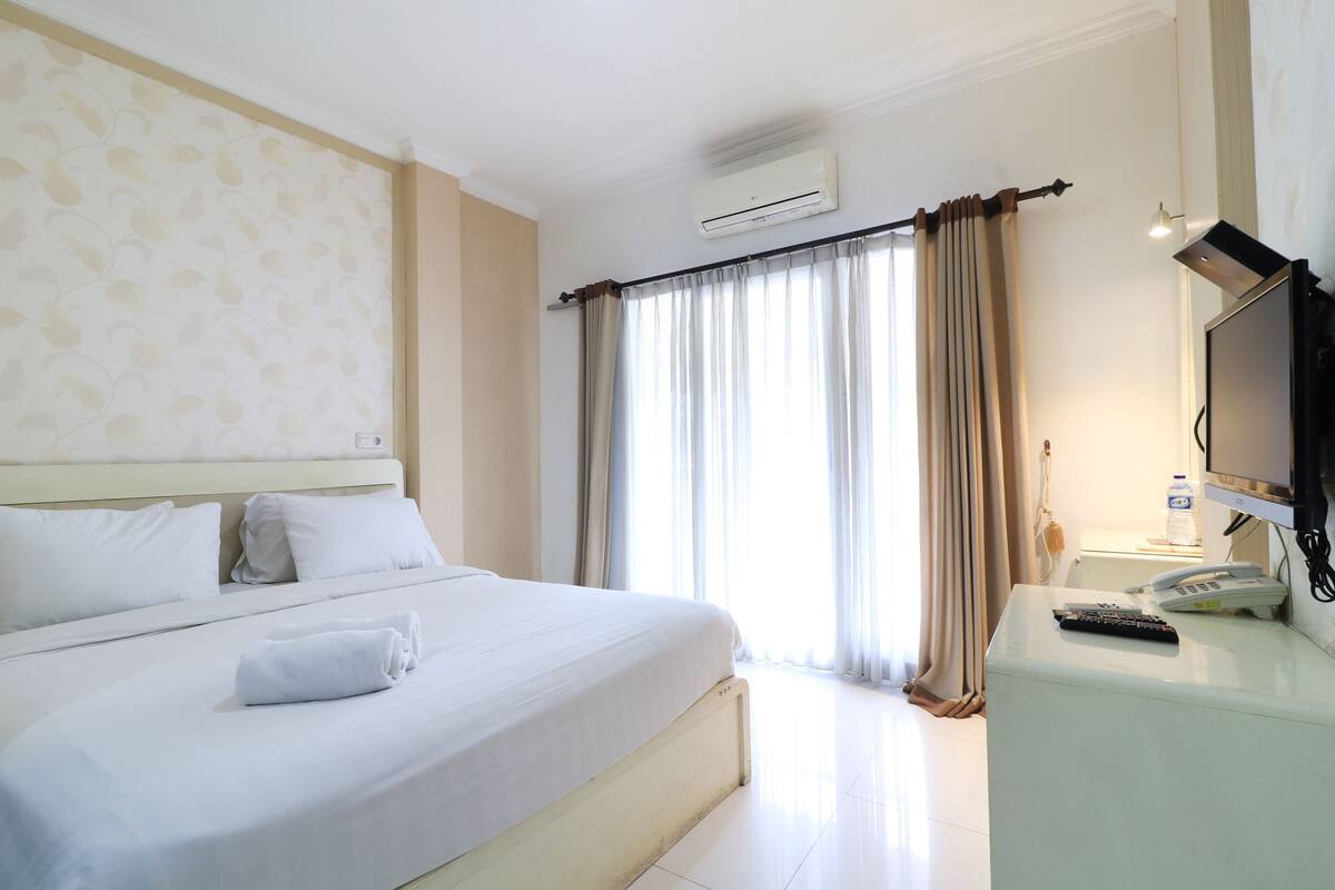 A hotel room with a bed, a desk with a telephone, and a television.