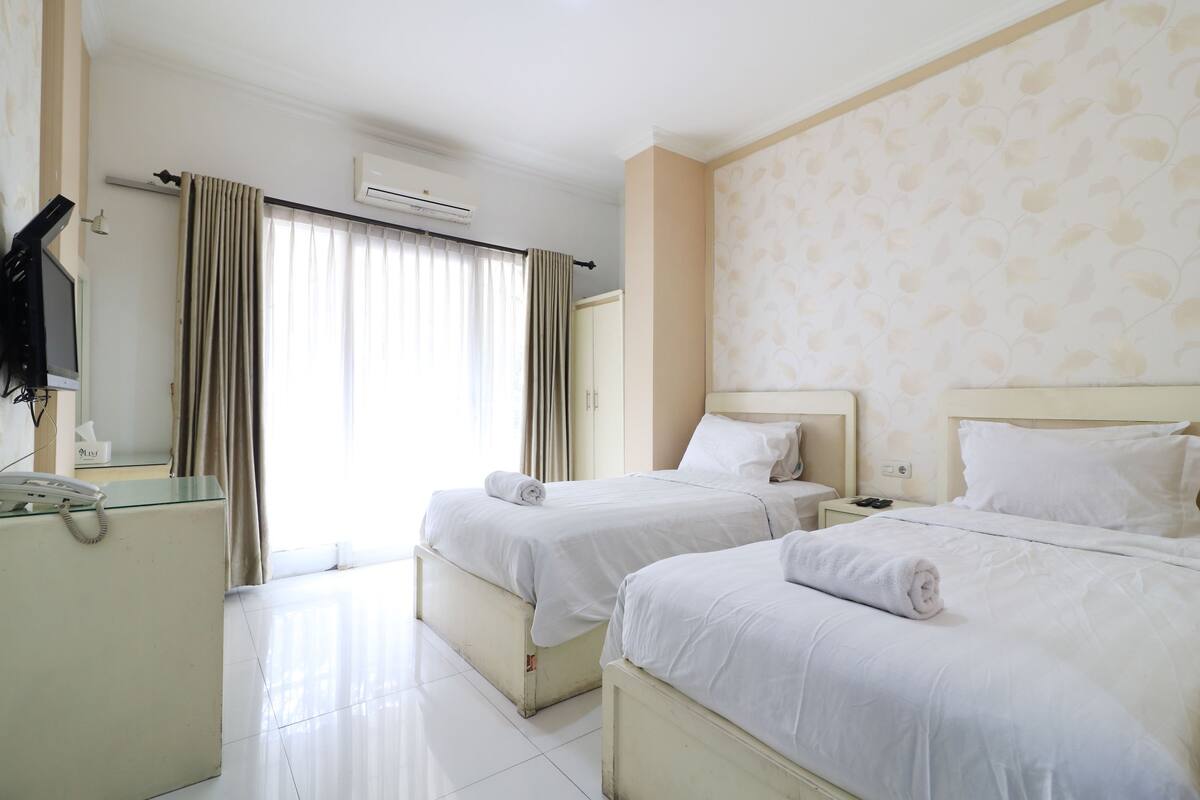 A hotel room with two beds, a desk with a telephone, and a television on the wall.