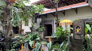 A courtyard with a traditional wooden door, a yellow umbrella, and a statue of a deity. - Chendana Homestay Bali (Denpasar)