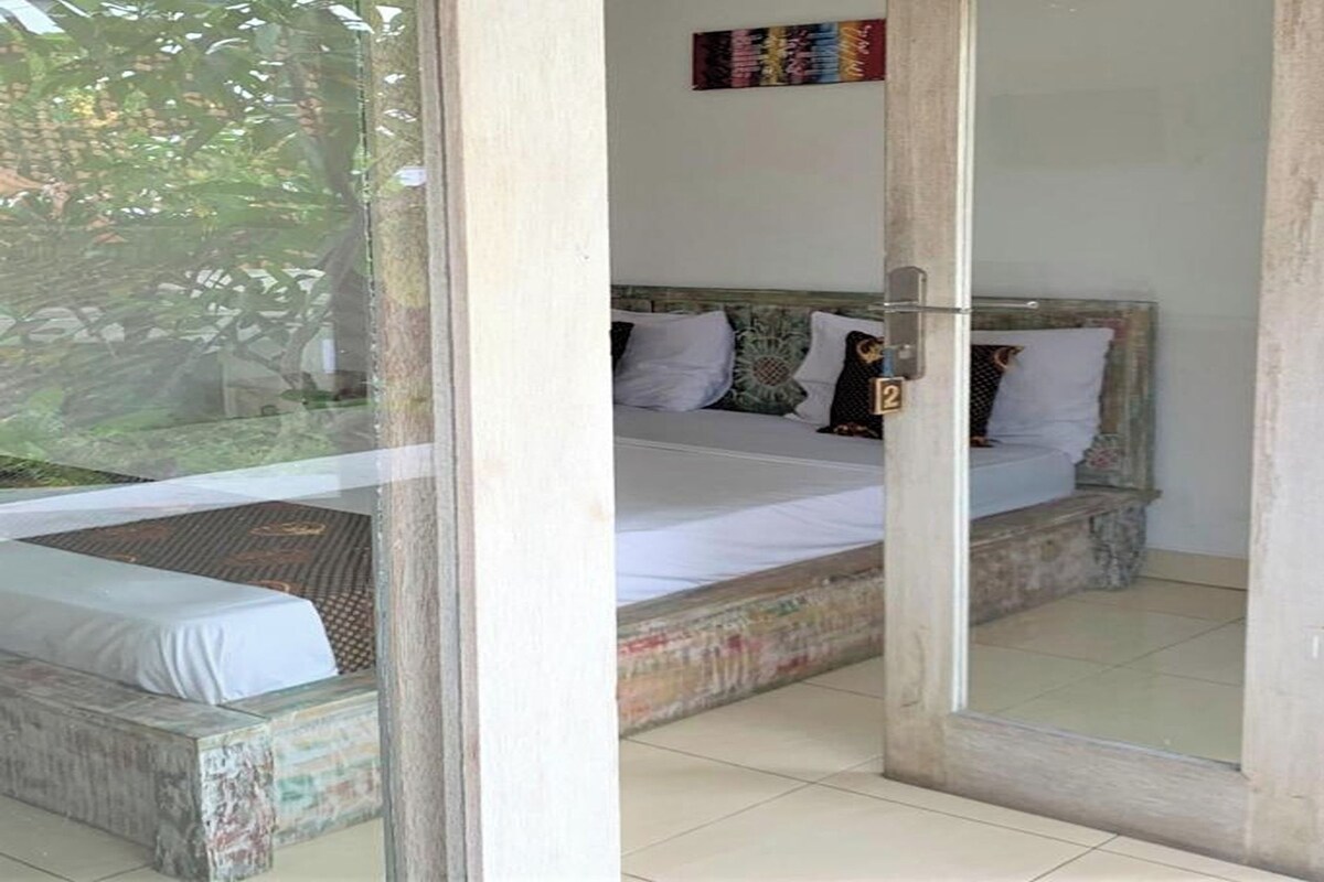 A bedroom with a bed, a small table, and a view of the outdoors.