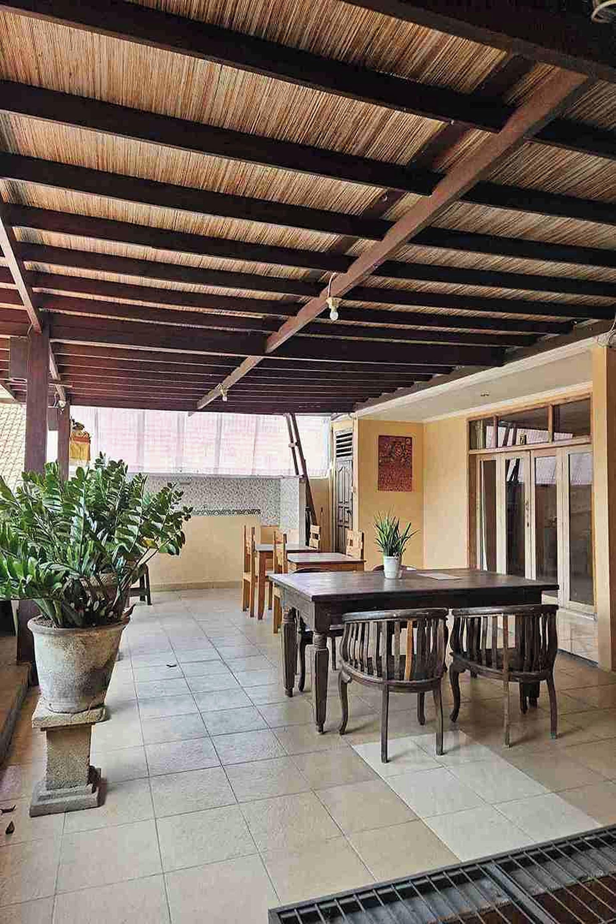 Un espace extérieur abrité, doté d’une table et de chaises, de plantes en pot et d’un sol carrelé.