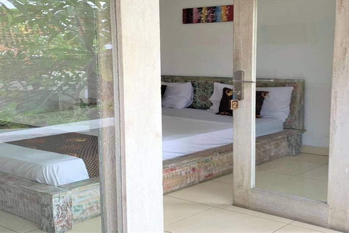 A bedroom with a bed, a small table, and a view of the outdoors.