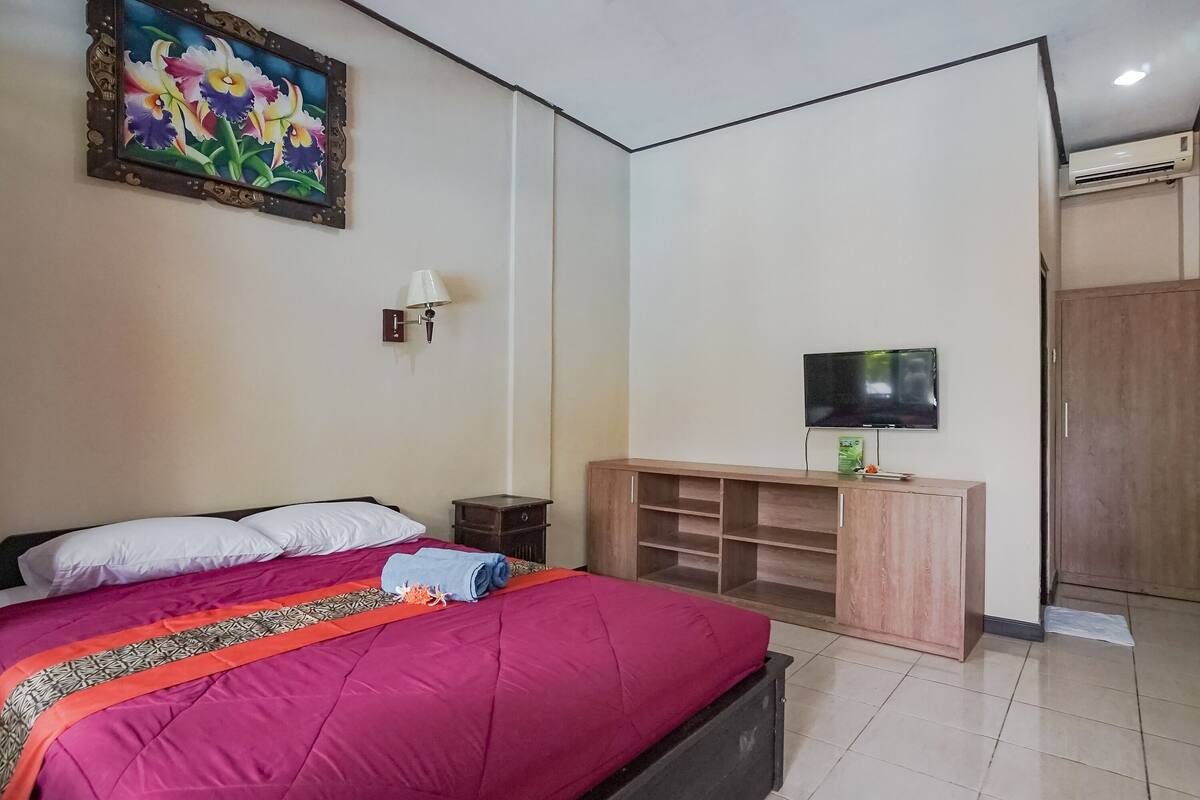 A bedroom with a large bed, a TV on a wooden cabinet, and a painting on the wall.