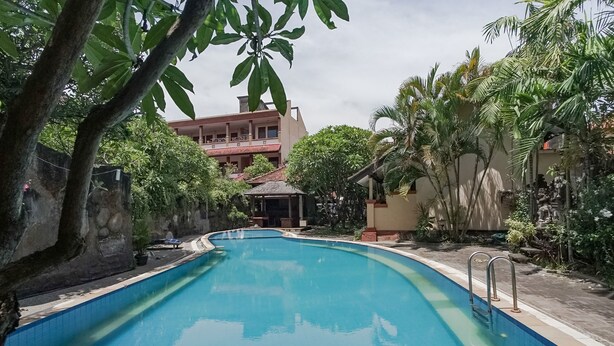 Una piscina rodeada de vegetación y un edificio con techo rojo.