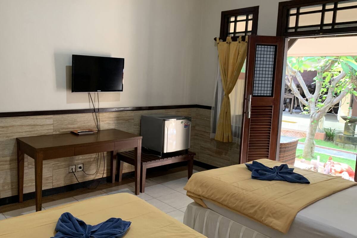 A room with two beds, a TV, a small fridge, and a window with curtains.