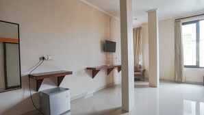 A spacious room with a flat-screen TV mounted on the wall, a small refrigerator, and a wooden shelf. - Taxa Uma Guest House (Kuta)