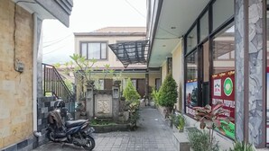 A narrow alleyway with a parked scooter, potted plants, and a building with a stone facade and large windows. - Taxa Uma Guest House (Kuta)