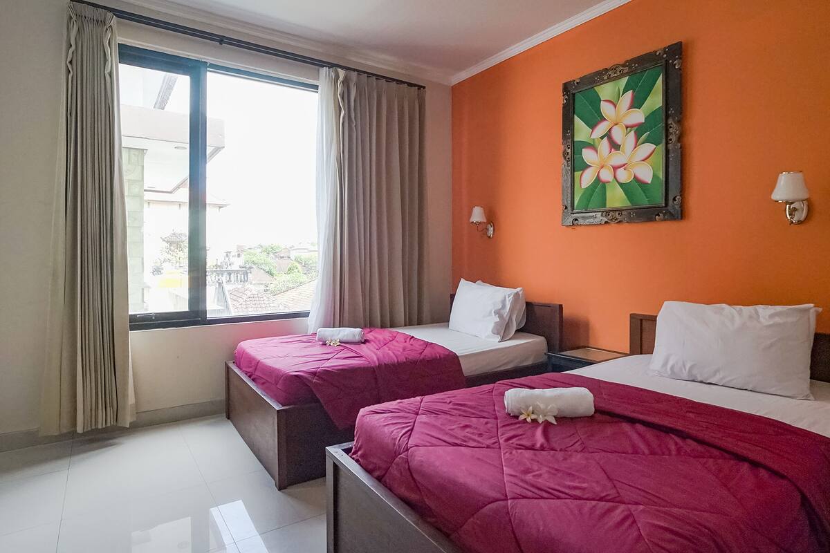 A hotel room with two beds, a large window with curtains, a painting on the wall, and a view of the outside.