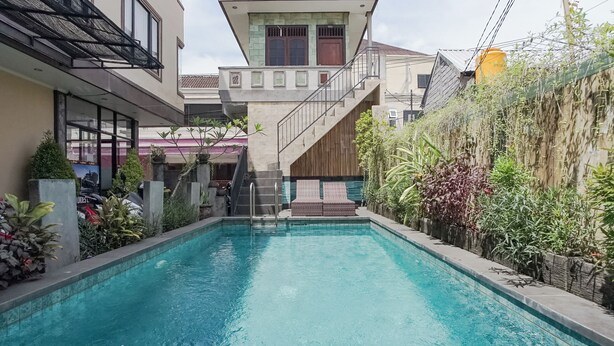 A swimming pool with a wooden deck and stairs leading to a house. - Taxa Uma Guest House (Kuta)