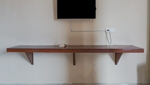A flat-screen TV mounted on a wall above a wooden bench. - Taxa Uma Guest House (Kuta)