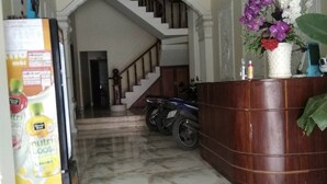 A reception area with a marble floor, a wooden reception desk, a staircase, and a refrigerator with a nutritional drink advertisement.