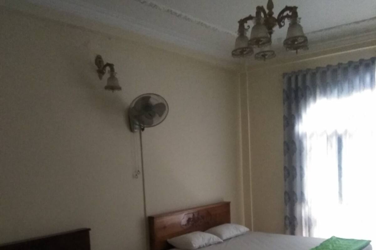 A hotel room with two beds, a ceiling fan, and a window with curtains.
