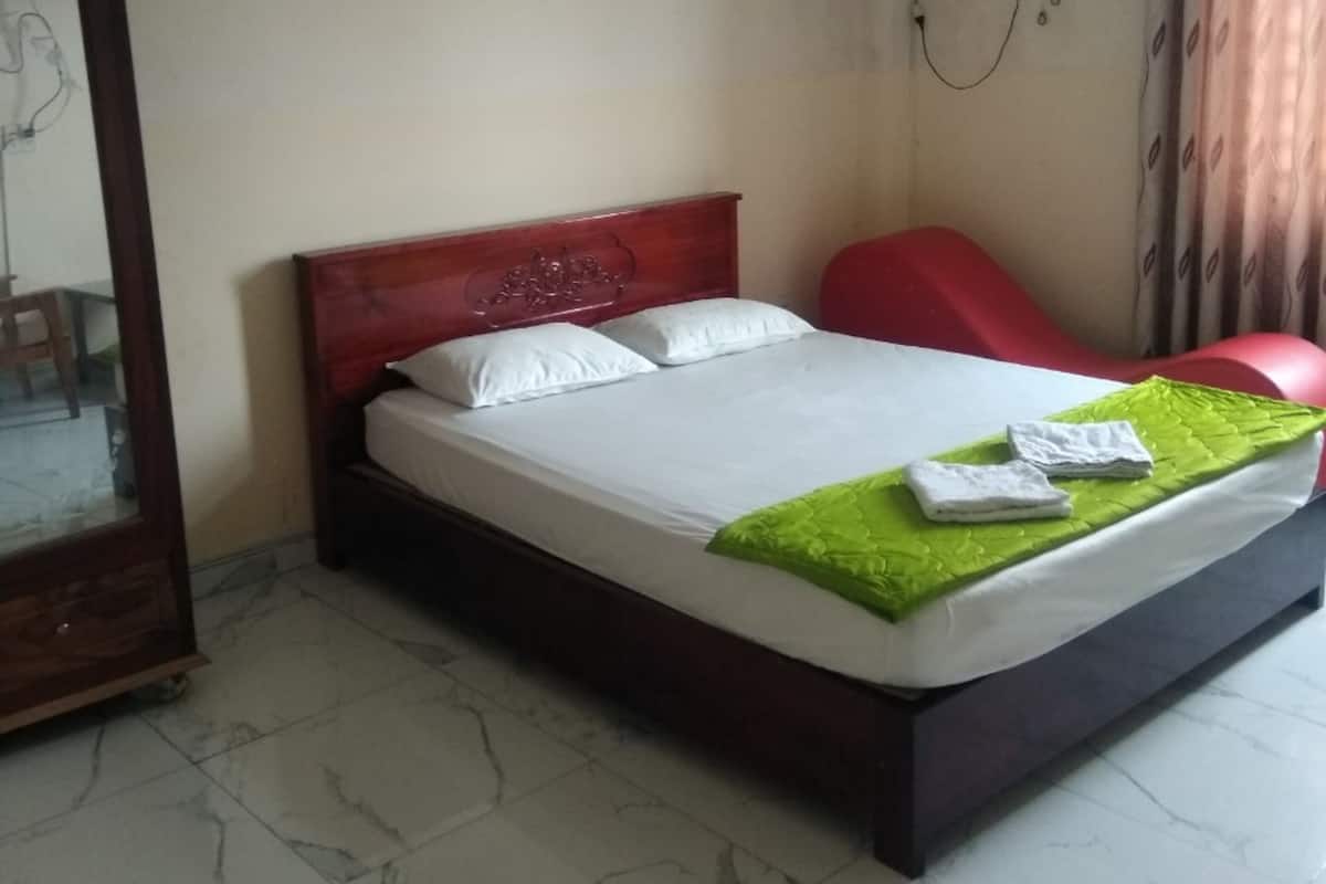 A bedroom with a bed, a red chair, a wooden wardrobe, and a wall-mounted air conditioner.