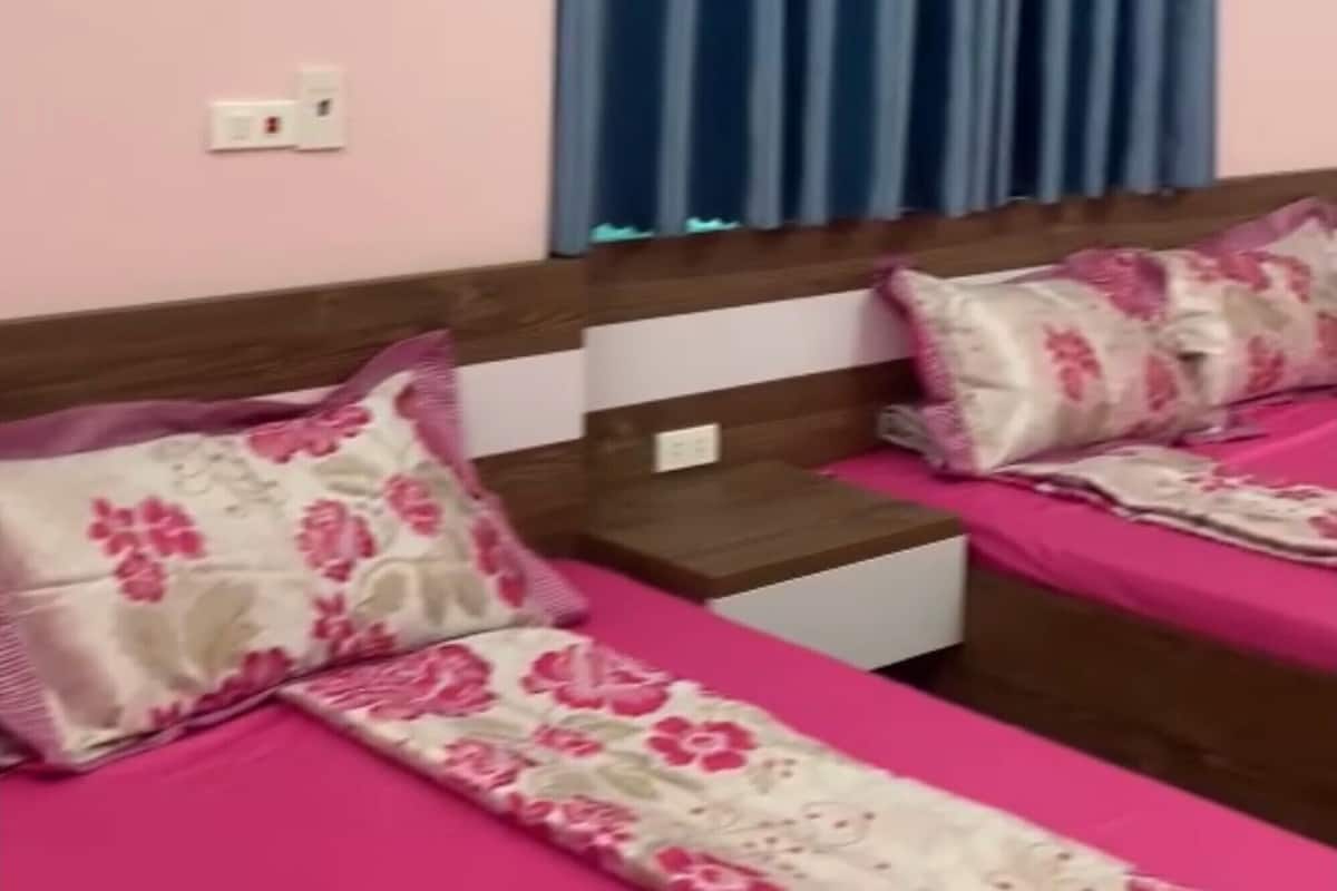 Une chambre avec deux lits, un ventilateur fixé au mur et une fenêtre avec des rideaux bleus.
