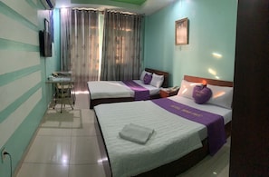 Habitación de hotel con dos camas, una mesita, una silla, un televisor y una ventana con cortinas.