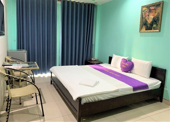Una habitación de hotel con una cama, un escritorio con una silla, un teléfono y un cuadro en la pared.