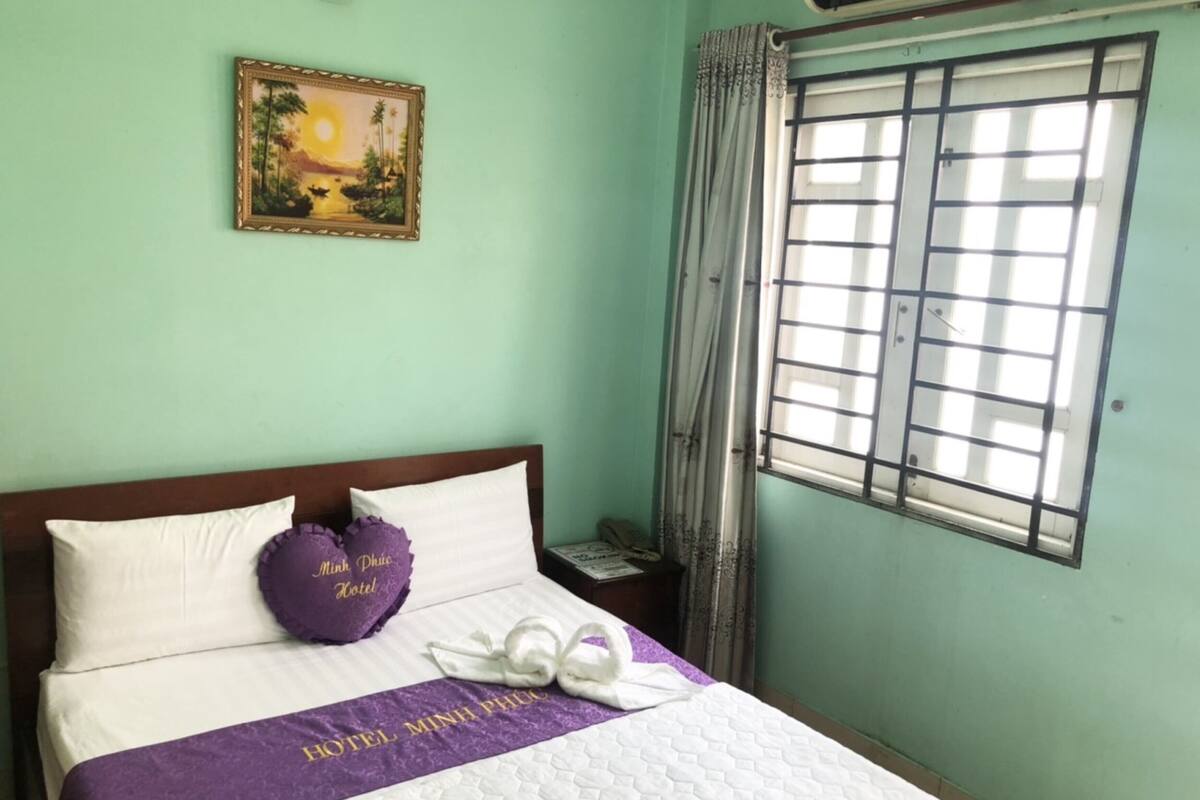 Une chambre d’hôtel comprenant un lit, une table de chevet, une fenêtre avec des rideaux et un climatiseur fixé au mur.