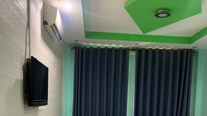 Une pièce avec un mur blanc, une serviette noire accrochée au mur, une fenêtre avec des rideaux foncés et un plafond vert et blanc doté d’un éclairage encastré.