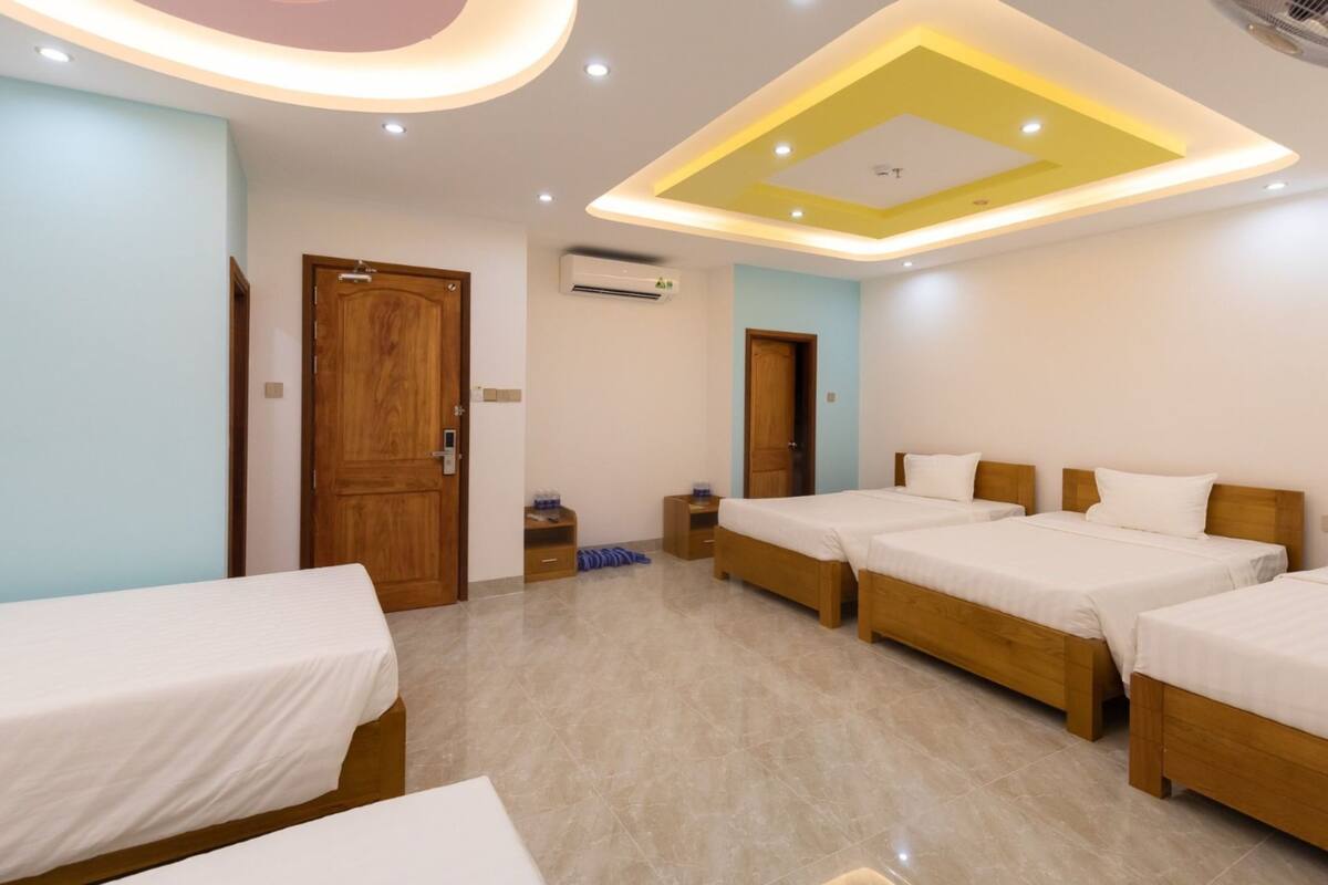 A hotel room with four single beds, a wooden wardrobe, an air conditioning unit, and a ceiling with recessed lighting.