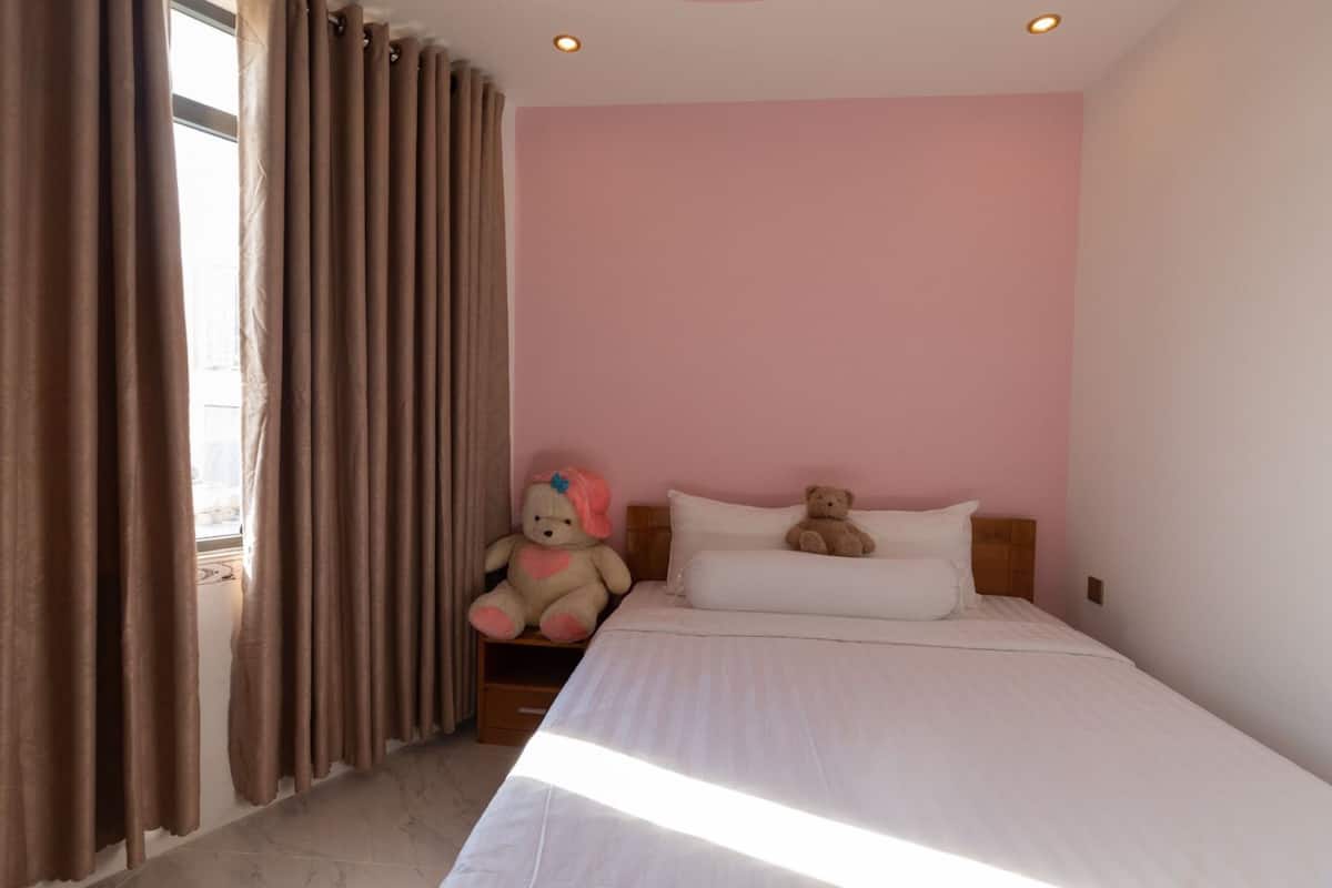 A bedroom with a bed, two pillows, a nightstand, and two teddy bears.